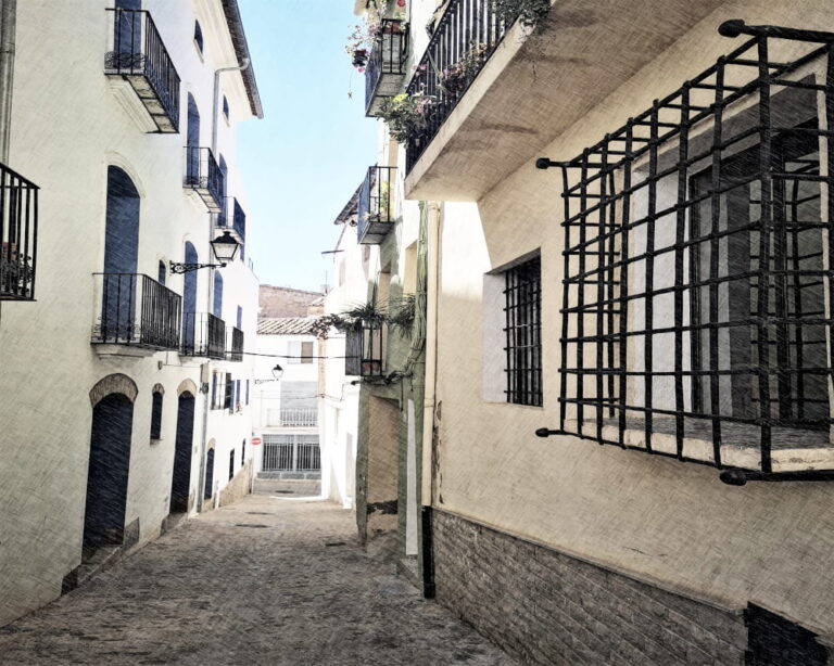 Apartamentos turísticos en Segorbe. Callejón empedrado con fachadas blancas y balcones de hierro forjado en el casco histórico de Segorbe, Castellón.